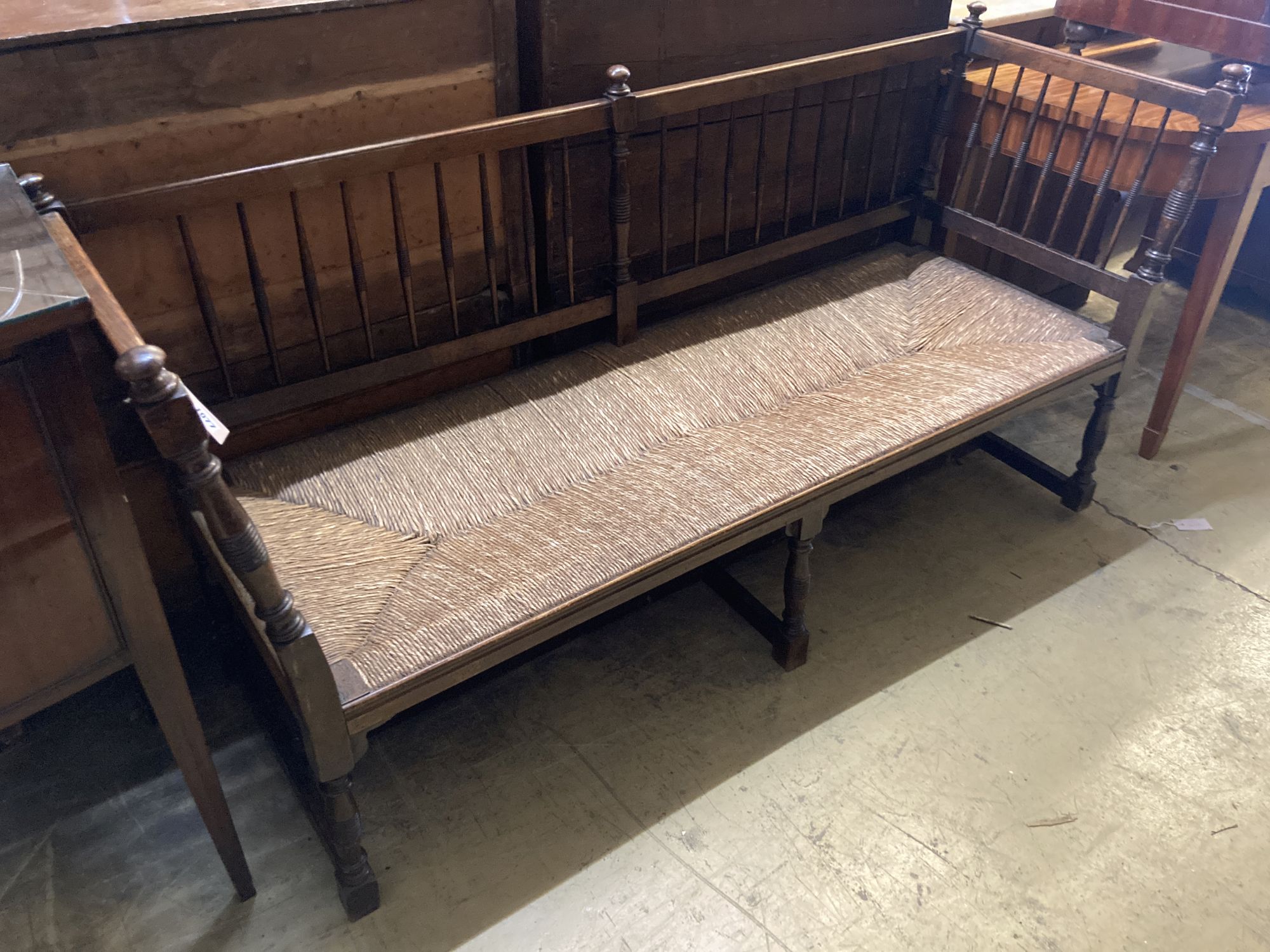 An Arts and Crafts oak framed rush seated settee, with turned supports and spindle back, length 166cm, depth 57cm, height 87cm